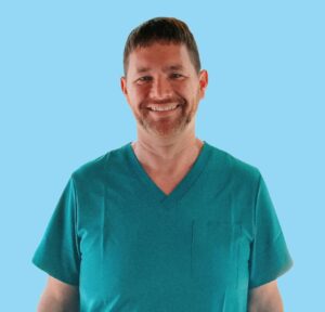 home wound care physical therapy Erie PA. Smiling healthcare professional in teal scrubs standing against a blue background, representing Breakwall Wound Care and Rehab's dedicated wound care and physical therapy specialist.